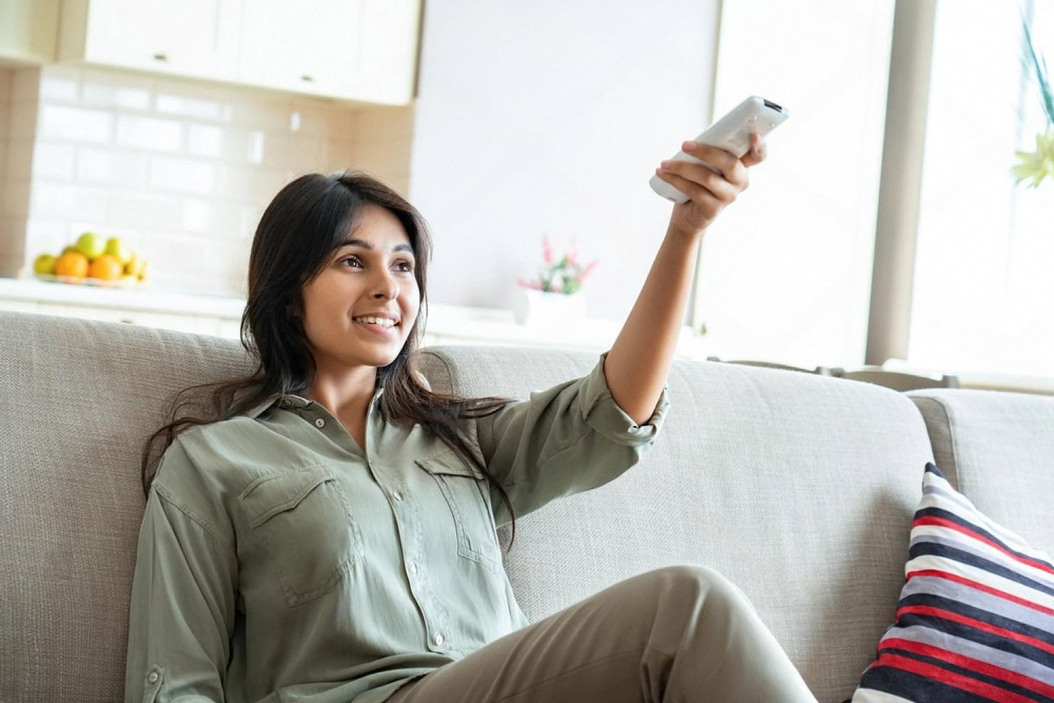 Woman on a sofa in a UAE apartment adjusting a portable air conditioner remote