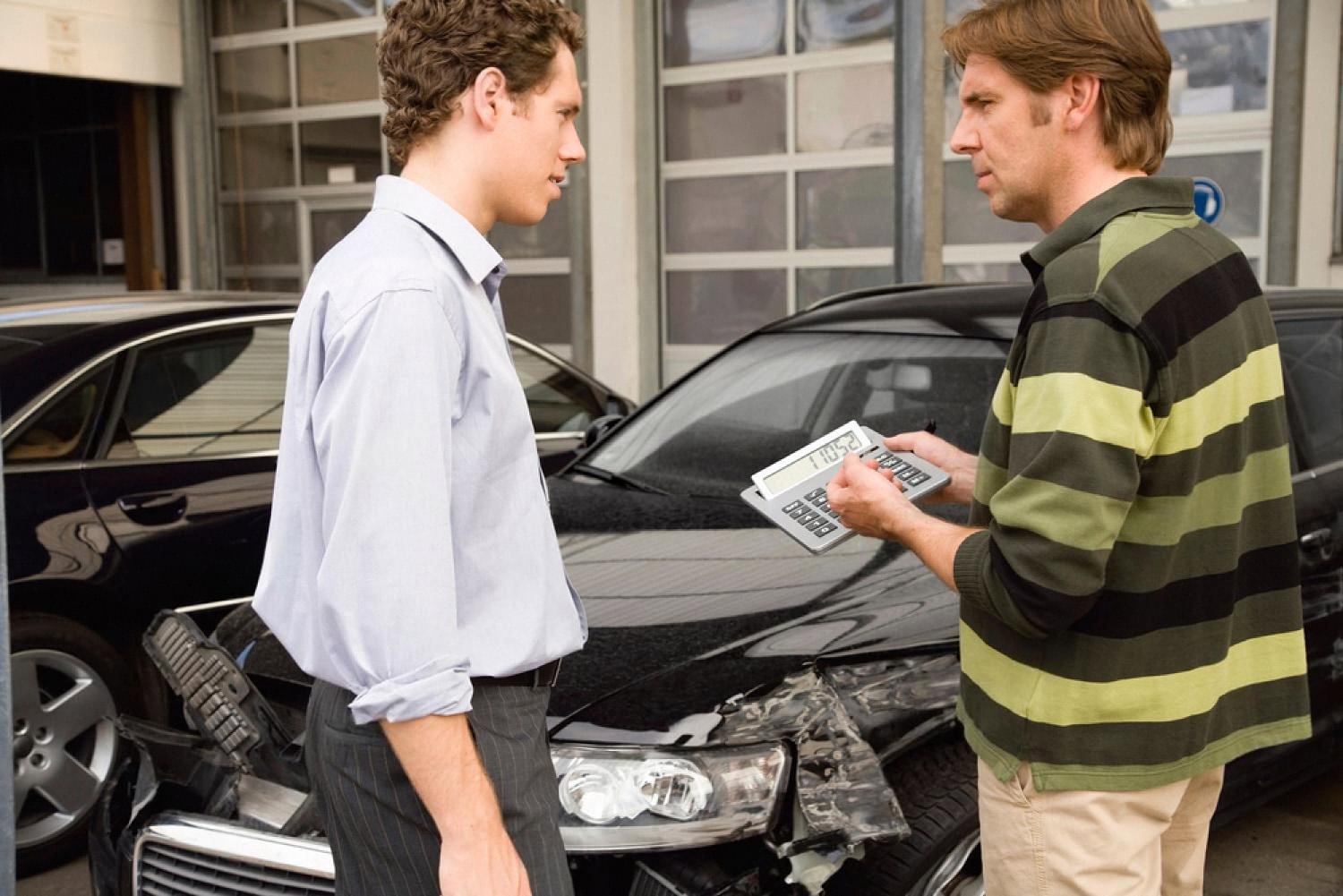 A UAE driver discussing a rejected insurance claim with an assessor next to a damaged car